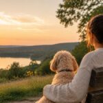 Nr. 1 Mensch Frau sitzt gemeinsam mit ihrem cremefarbenen Maltipoo auf einer Bank und blickt in die Natur.